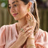 Woman wearing gold jewelry including earrings, rings, and a bracelet with a blurred green background.